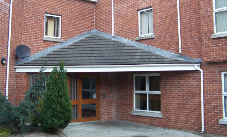 A brown wooden door set within a red brick building, sheltered by an overhead roof.