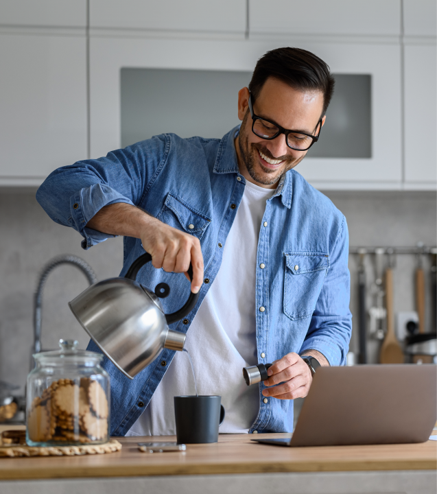 Man smiling while pouring water from a kettle into a mug