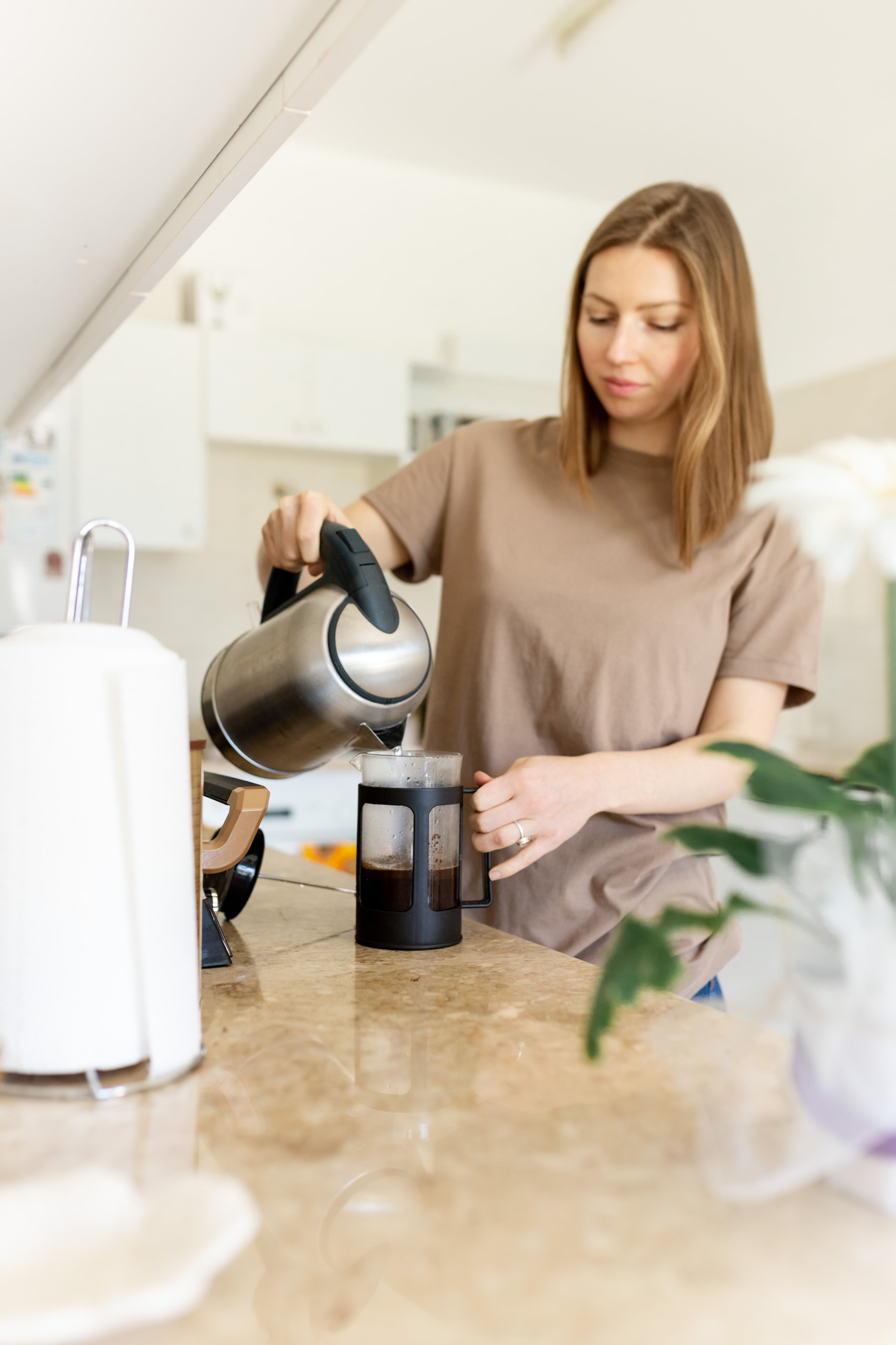 Young woman sanding at kitchen counter, pouring herself a cup of hot coffee, enjoying leisure time at home in the morning